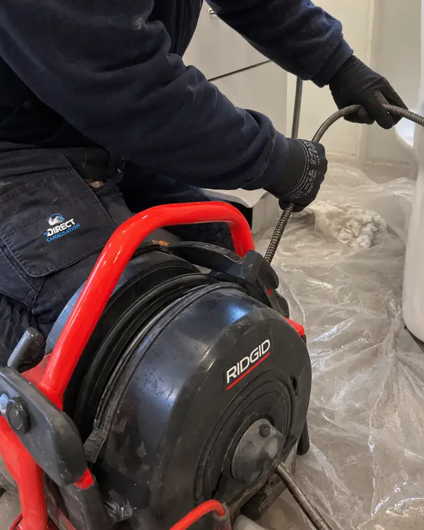 Technicien utilisant un furet électrique sur une cuvette de WC