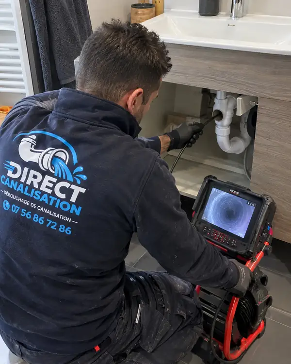 Technicien Direct Canalisation inspectant une canalisation avec une caméra sous un lavabo